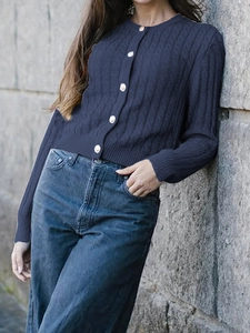 Detailed close-up of blue cable knit cardigan featuring classic white buttons and soft texture
