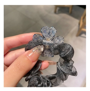 Macro detail of a sparkling rhinestone clover charm on a grey metallic mesh scrunchie