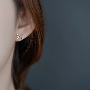 Close-up of a silver bow knot earring worn by a model in a minimalist setting