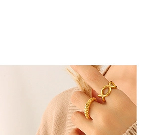 Close-up of golden infinity and croissant rings worn on hand against beige knitwear