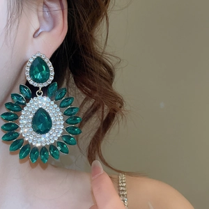 Close-up of vintage emerald green teardrop earrings with halo diamond setting on model