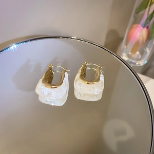 Detail of U-shaped earrings featuring gold metal and creamy marble resin on a mirror