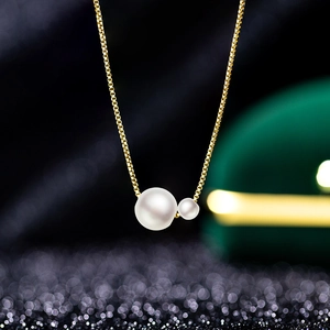 Macro shot of twin pearls pendant featuring golden box chain with detailed metallic texture
