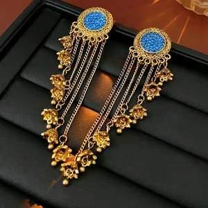 Detail of gold tassel earrings with blue rhinestones and floral charms on a black tray