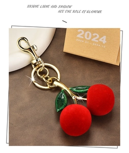 Macro shot of dark red flocked cherries keychain with glitter green leaves and gold hardware