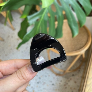 Detail shot of a small black glossy cat ear claw clip held against a leafy green plant