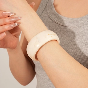 Detail of wide cream resin bangle with marble texture worn on the wrist for a soft look