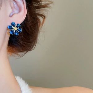 Detail of flower stud earrings featuring dark blue teardrop stones and yellow center