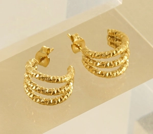 Detailed close-up of gold U-shaped earrings with unique textured finish on acrylic stand
