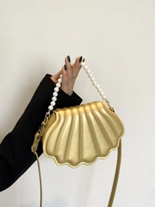 Detail view of a gold shell-shaped handbag featuring a luxury pearl bead handle accessory