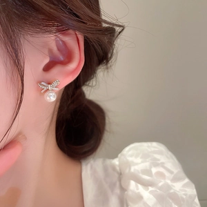 Gros plan de boucles d'oreilles nœud dorées avec zircons et perle portées par mannequin