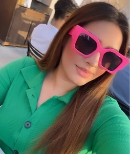Detail of trendy pink square frame sunglasses worn with green knit sweater in a selfie