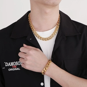 Détail d'un ensemble collier et bracelet gourmette dorés pour homme sur chemise noire