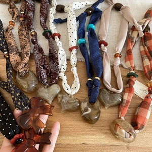 Detailed flat lay of fabric bow and acrylic heart pendant necklaces on linen surface
