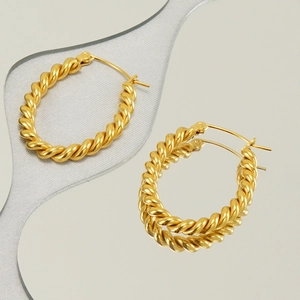 Polished 18k gold plated twisted hoop earrings reflecting on a mirror surface