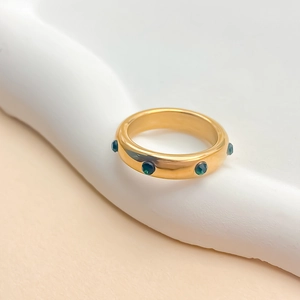 Détail d'une bague dorée 18 carats avec pierres vertes incrustées sur un plateau blanc