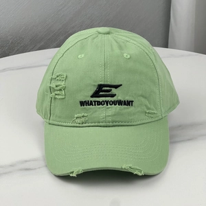 Detail of mint green baseball cap featuring black embroidery and distressed ripped texture