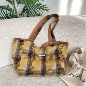 Detail shot of yellow and brown plaid tote bag with brand label on a cozy beige sofa
