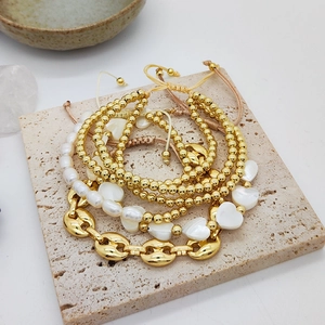 Mehrlagiges goldfarbenes Perlenarmband-Set mit weißem Herzanhänger auf Naturstein