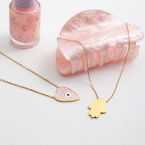 Detail of 18K gold stainless steel necklaces with pink enamel heart and Hamsa hand charms