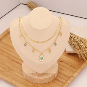 Double-layered gold necklace featuring turquoise pendants and leaf charms on a bust display