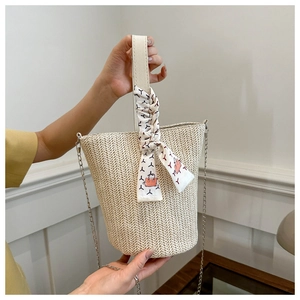 Détail du sac seau en paille tressée avec anse en cuir blanc et accessoire foulard en soie