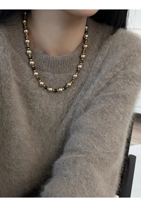 Détail du collier de perles dorées champagne et oeil de tigre sur un pull en mohair brun