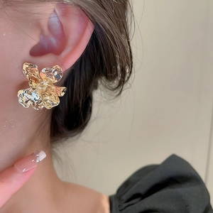 Detail of gold floral earring with hammered metal texture worn on a female model
