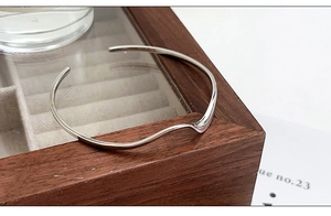 Dettaglio di un bracciale rigido in argento ondulato su una scatola di legno scuro