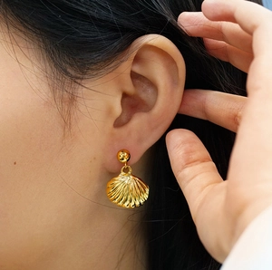 Close-up of a golden seashell earring showing textured metallic details on a model