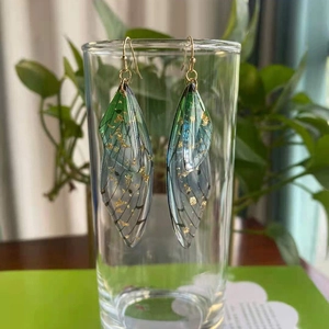 Macro detail of gradient green cicada wing earrings with gold foil and metal hooks