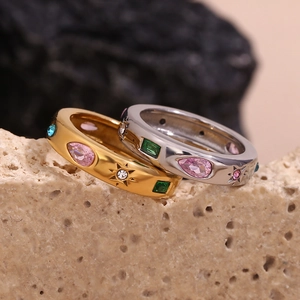 Detail of gold and silver rings with colorful gemstones on a textured beige stone