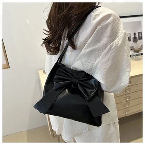 Detail of a black leather shoulder bag featuring a large decorative bow on the side