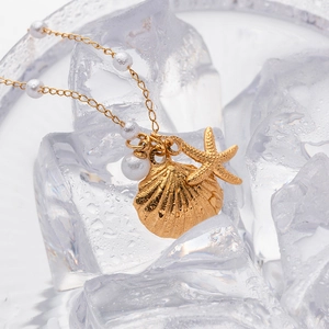 Detail of gold starfish and conch pendant necklace with white pearls on ice background