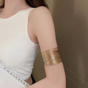 Detailed close-up of a layered gold wire arm cuff worn on an upper arm over white fabric