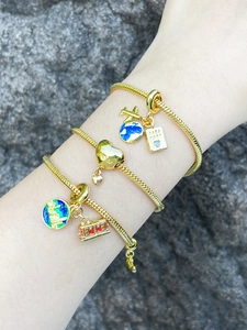 Detail of travel-themed gold snake chain bracelets with passport, airplane and globe charms