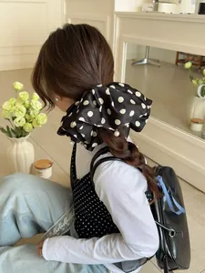 Detail of oversized black polka dot satin bow hair tie with elegant white pearl pendant charms