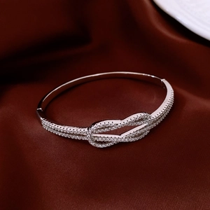 Détail d'un bracelet nœud argenté avec zircons étincelants sur fond de soie rouge