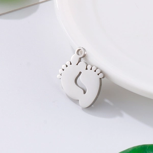 Polished stainless steel baby footprints pendant on white surface with leaf background