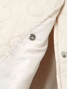 Detailed macro view of cream floral quilted jacket featuring silver metal snap buttons