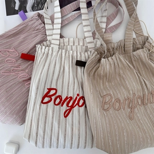 Detail of striped canvas tote bags featuring Bonjour embroidery and thick rope handles