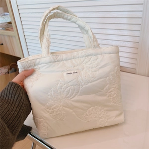 Detailed view of white quilted tote bag with lace floral embroidery and simple wish label