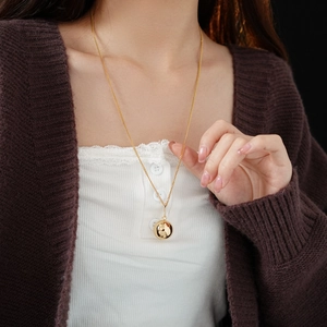 Close-up of a minimalist gold sphere pendant necklace worn by a model on dark background
