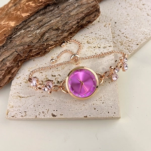 Close-up of rose gold bracelet watch with pink gemstones on a natural stone base