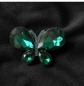 Macro shot of butterfly brooch with green crystals and blue rhinestones on black velvet