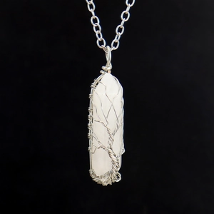Macro detail of hand-wrapped tree of life silver wire on white hexagonal crystal pendant