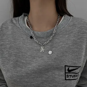 Detail of silver double-layered chain necklace featuring bear, black ring, and smiley charms