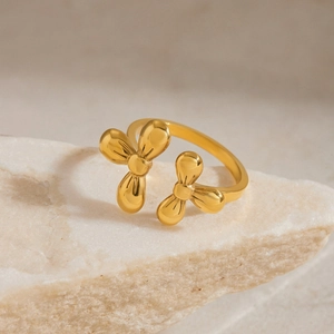 Macro detail of adjustable golden floral metal ring on a natural beige stone pedestal