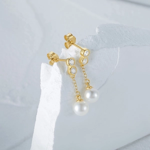 Detail of gold asymmetric S925 earrings with sparkling zircons and dangling pearls