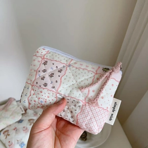 Hand holding a mini quilted floral coin purse with a pink zipper and woven label detail